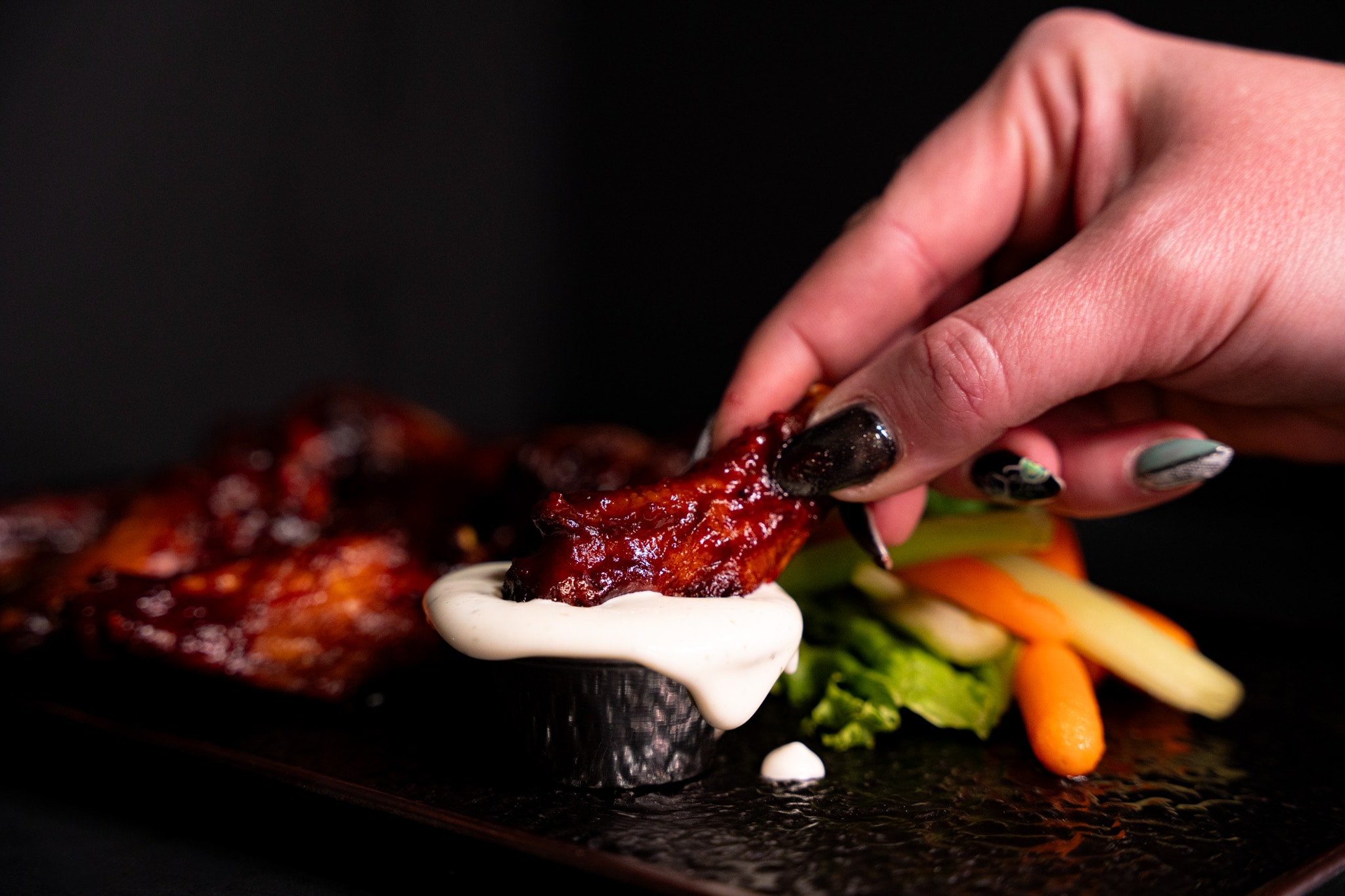 Glazed wing lifted from a plate of chicken wings